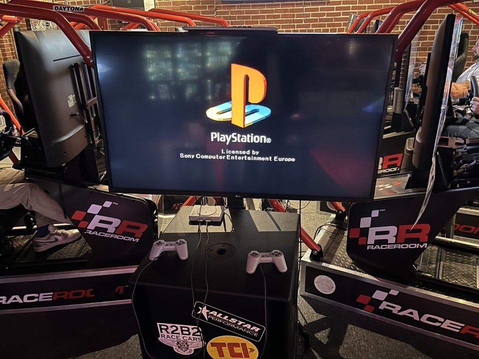 PlayStation with controllers between the racing rigs